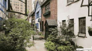 A view through the ornate gate into Pomander Walk NYC, showing charming Tudor style buildings and a cobblestone path.