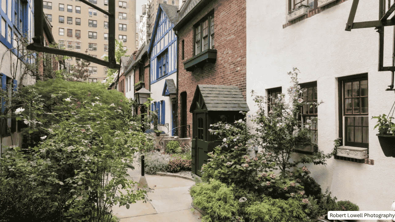 A view through the ornate gate into Pomander Walk NYC, showing charming Tudor style buildings and a cobblestone path.